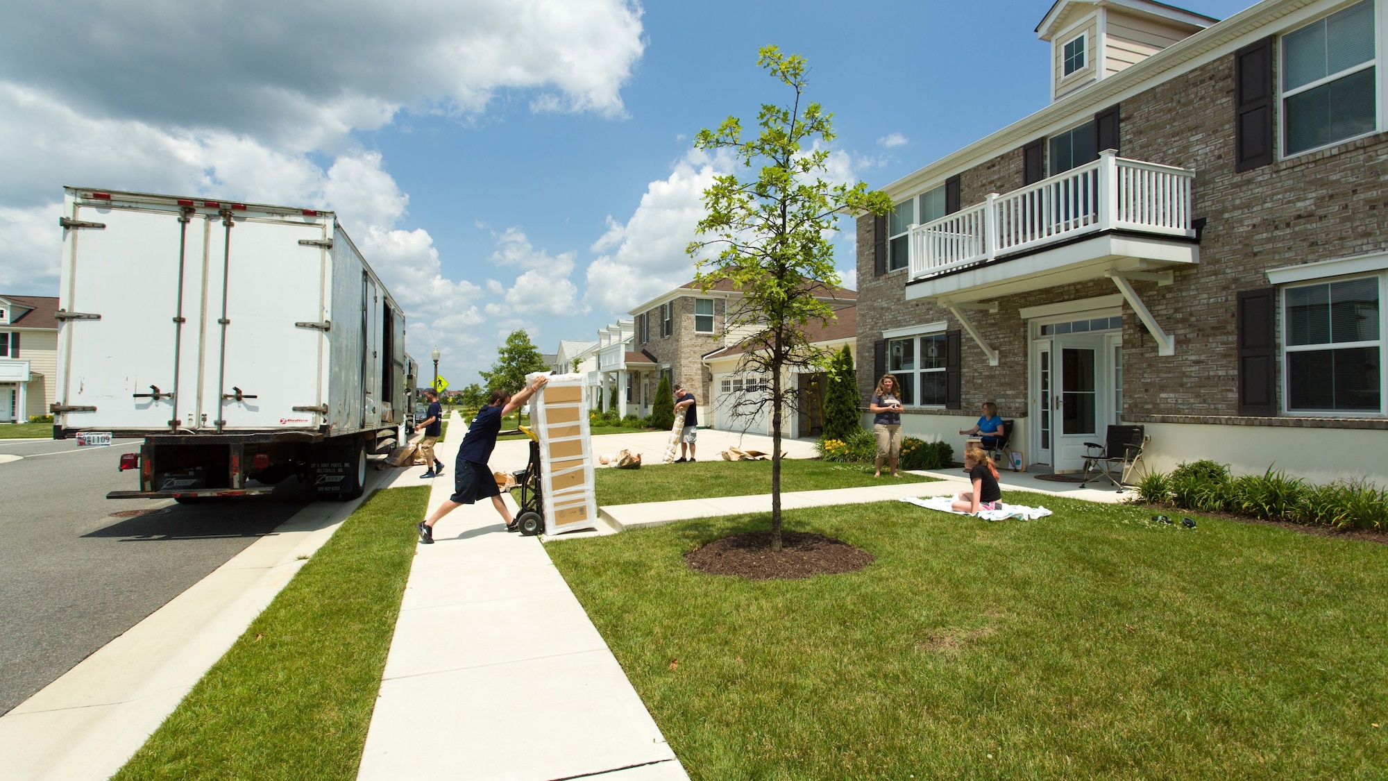 Photo of a moving company moving crates into a house while family members watch in the background.