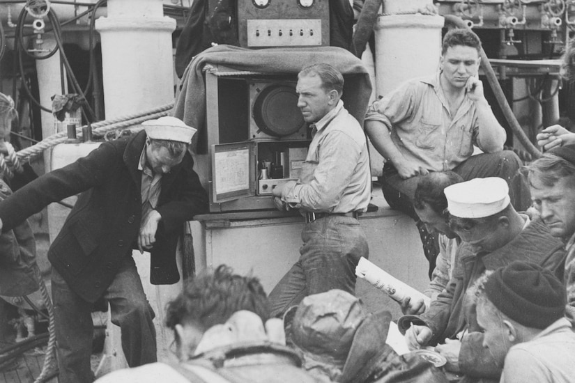 Men on a ship stand around communications equipment.