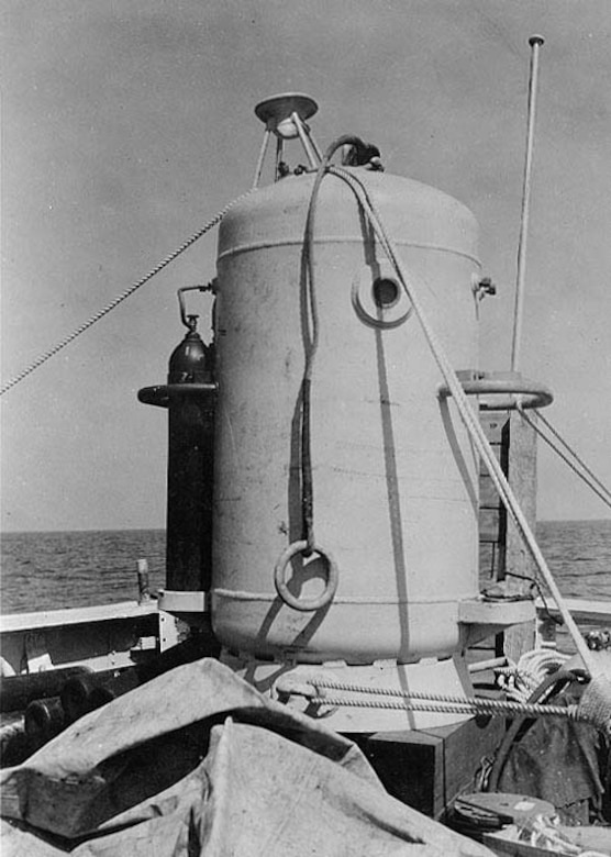 A large chamber sits tied down on a ship.