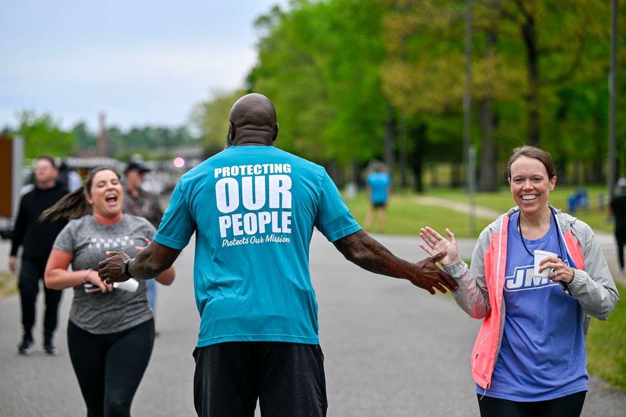A person in athletic attire offers encouragement to two runners also wearing athletic attire.