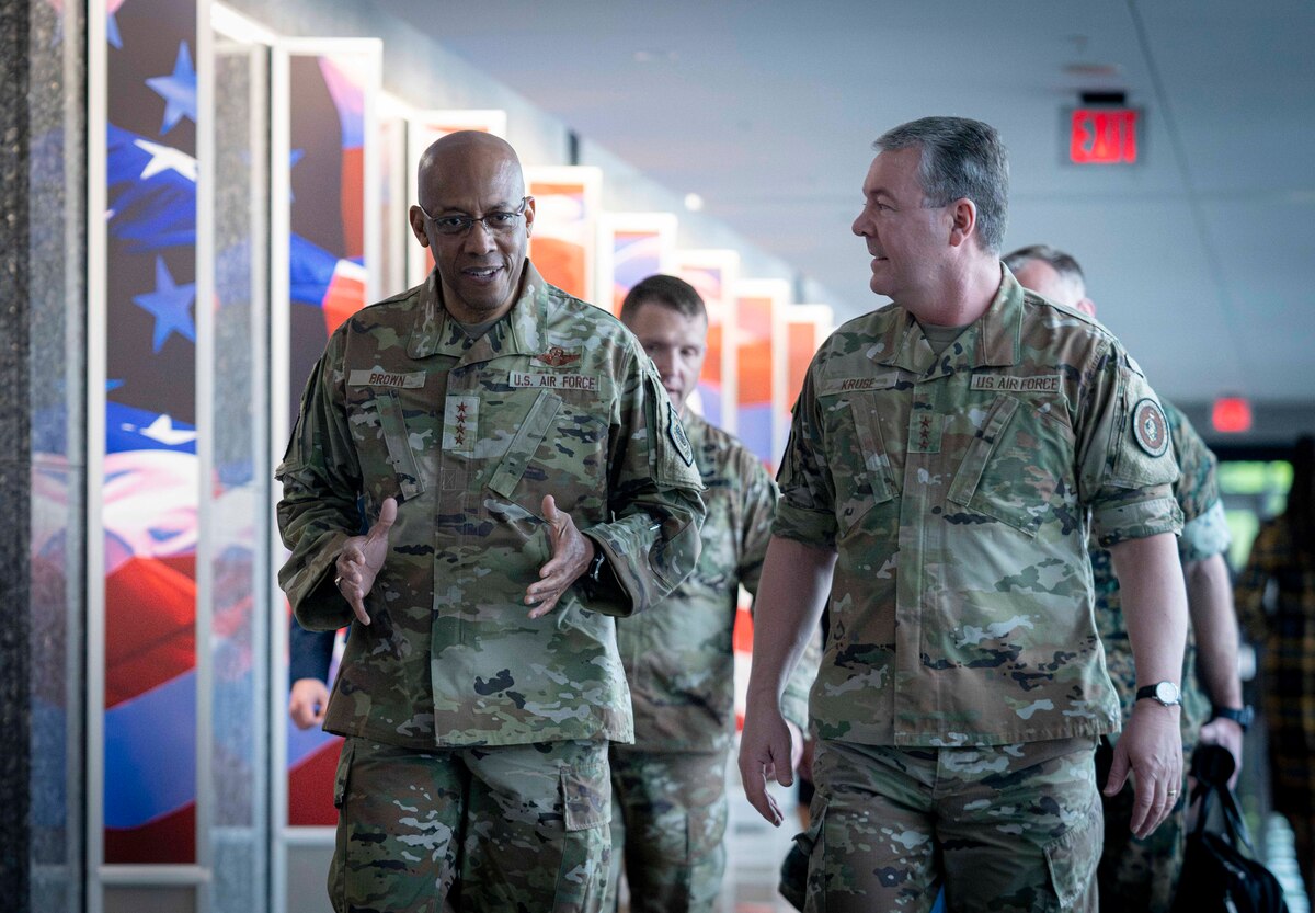 Two men in military uniform walk down a hall. Other service members walk behind them.