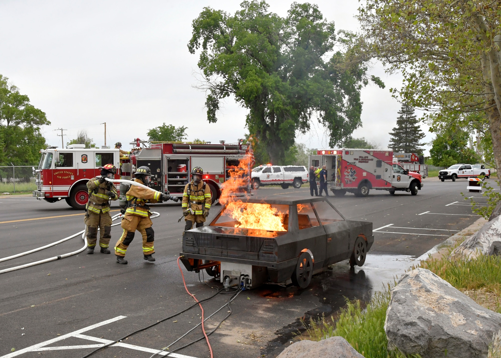 Three firefighters attack a simulated car fire.