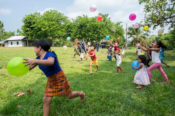 A photo of a lot of kids running and holding balloons in a grassy area.