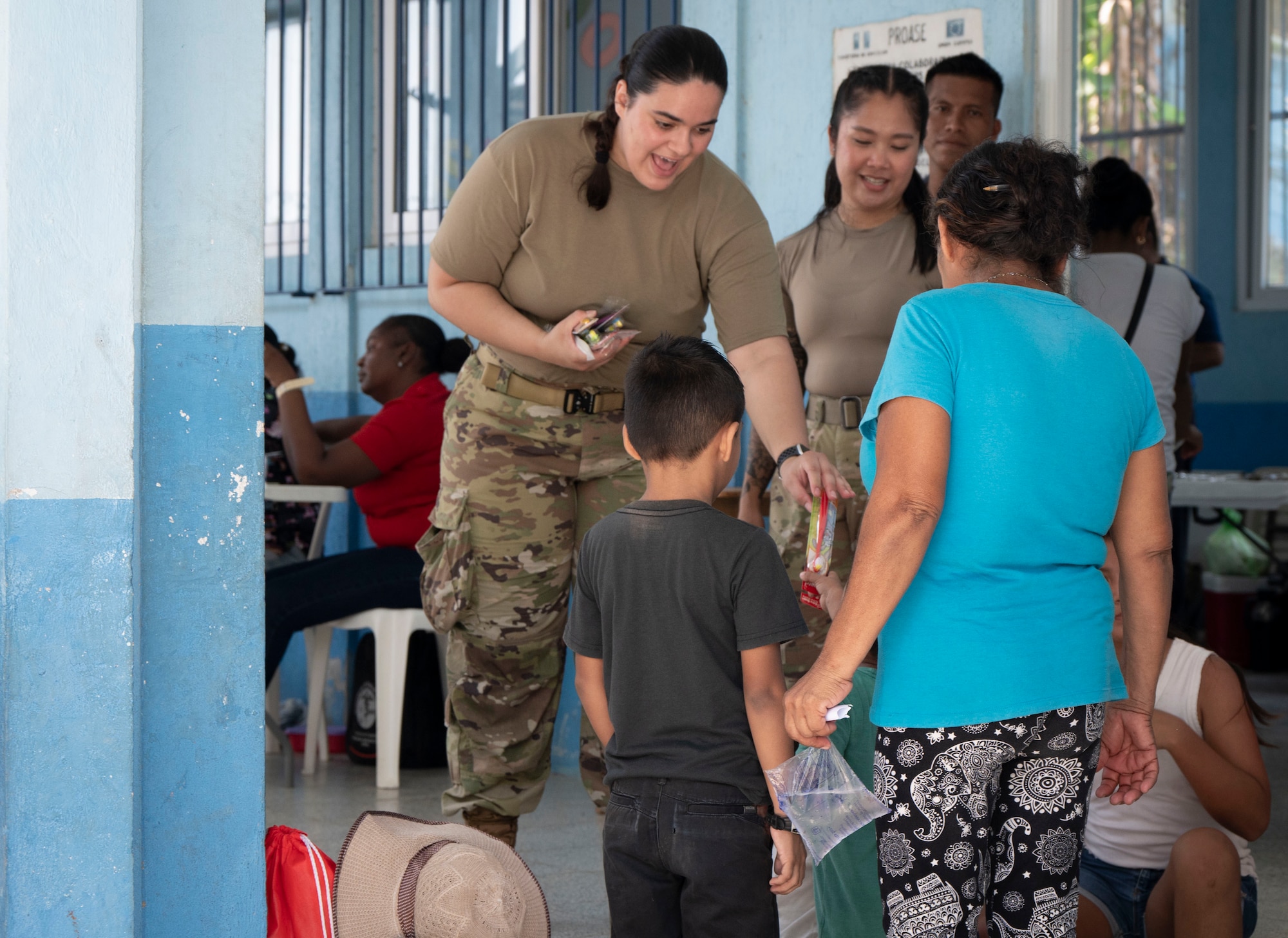 A photo of a military member handing a toothbrush to a mom and her sons while smiling.