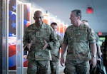 Two men in military uniform walk down a hall. Other service members walk behind them.