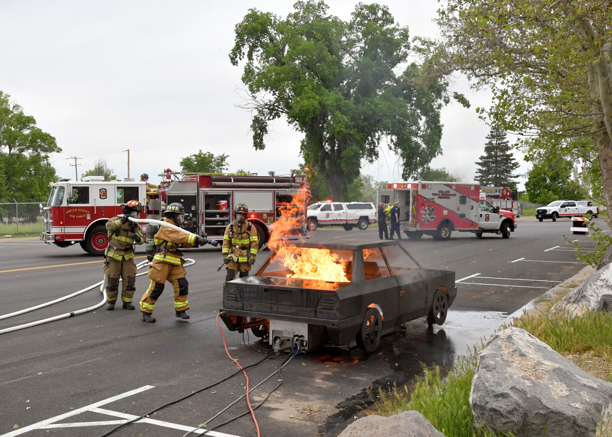 Three firefighters attack a simulated car fire.