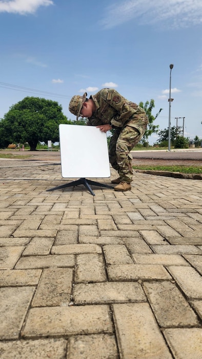 One uniformed U.S. Air Force Airman positions a piece of a equipment on a sidewalk.