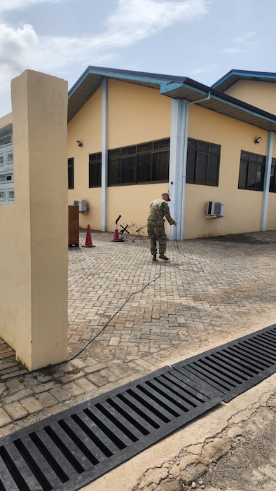 A black cord on a sidewalk leads up to a uniformed U.S. Air Force Airman configuring equipment on a sidewalk.