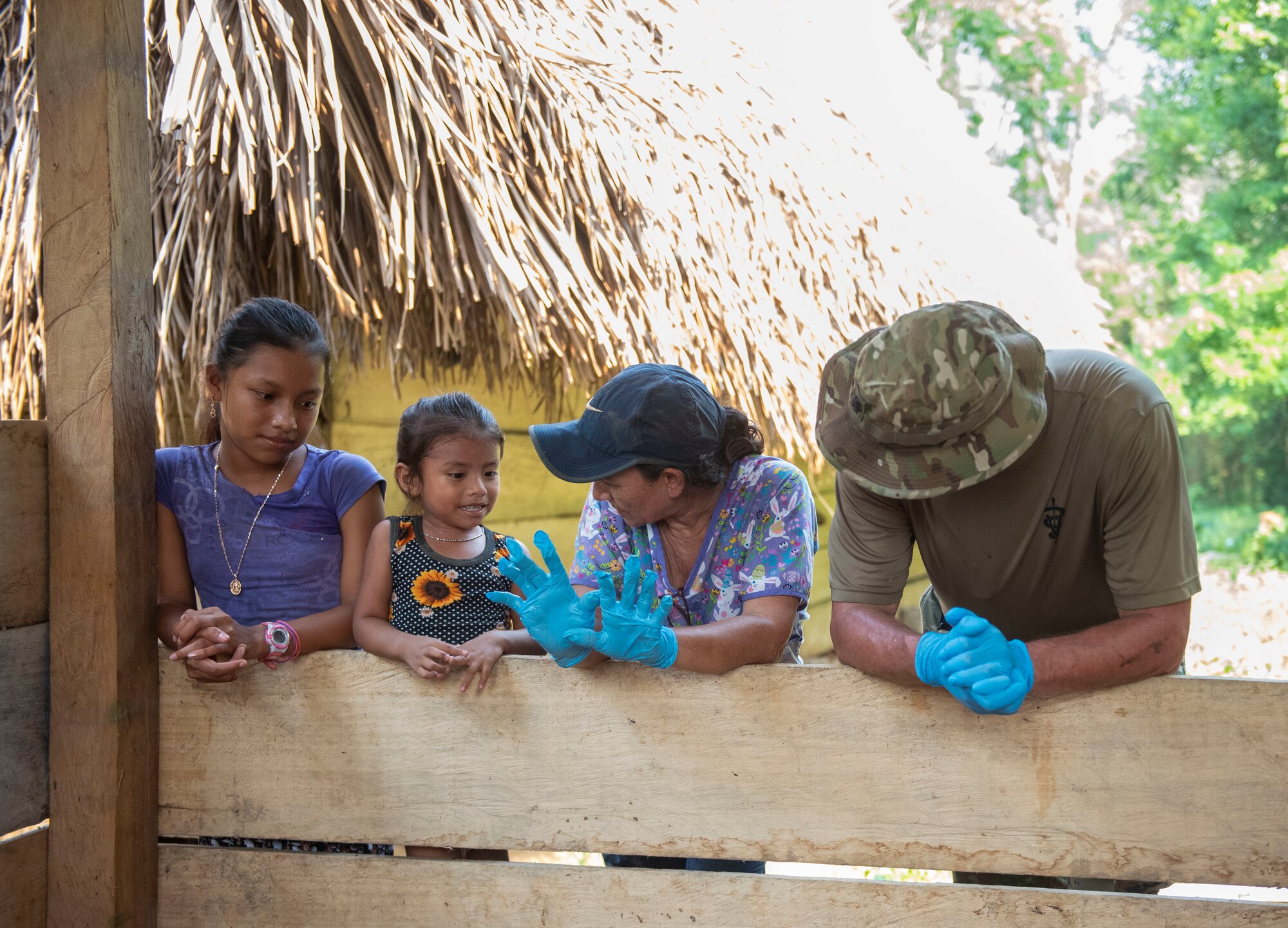A photo of two local kids talking to a woman and a military member while leaned over a fence.
