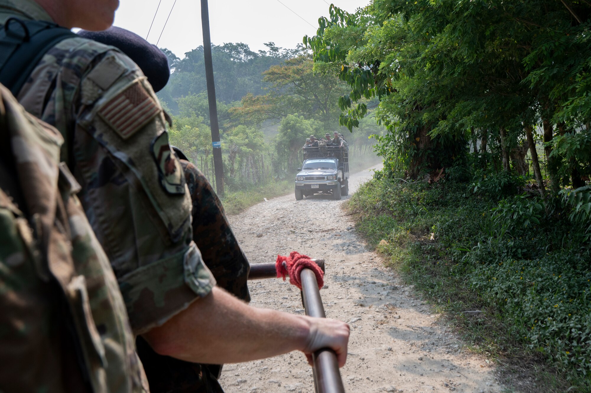 A photo of military members riding in the back of a truck facing another vehicle full of members following behind them.