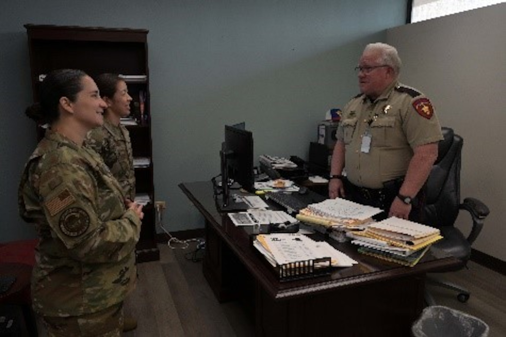 Three people standing around a desk having a conversation.