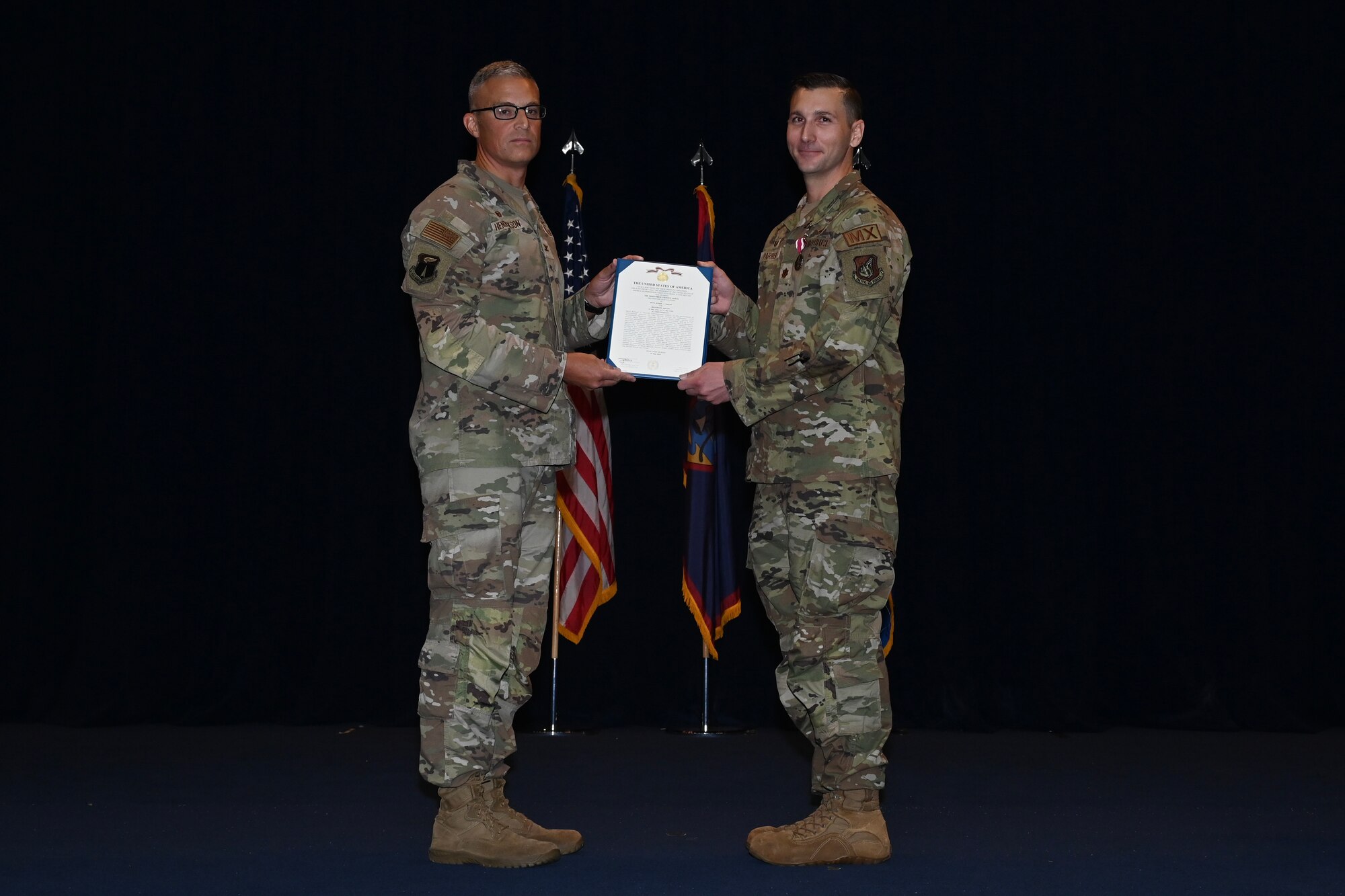 The 36th Maintenance Group commander, presents the meritorious service award certificate to the outgoing 36th Maintenance Squadron commander while standing on stage.