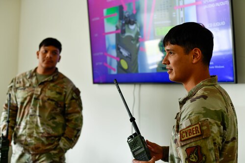 Two airmen stand by a television, with on holding a radio.