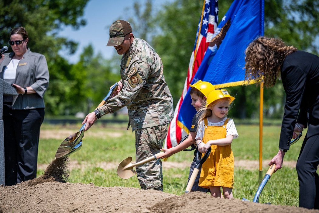 Chief Master Sgt. Morales shovels dirt beside two children wearing hard hats