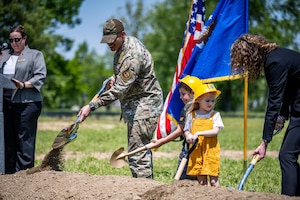 Chief Master Sgt. Morales shovels dirt beside two children wearing hard hats