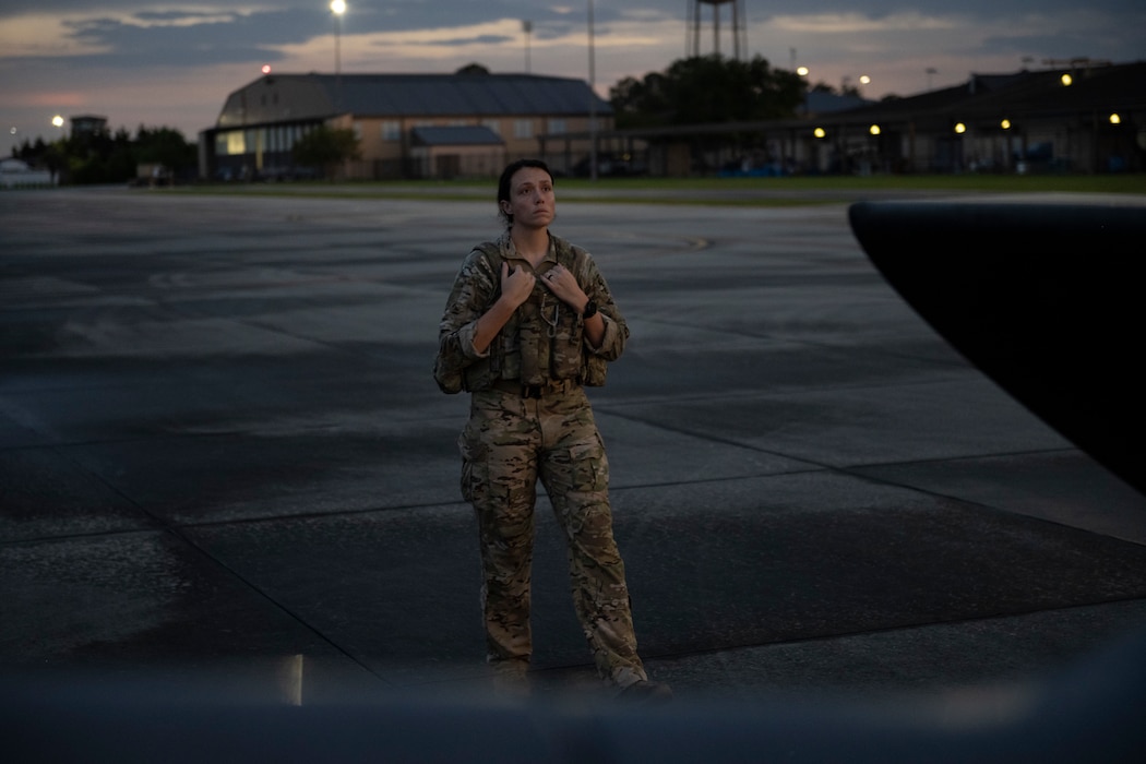 A photo of a person standing next to a helicopter, with her hands grasping the top of her vest as she looks at the helicopter.