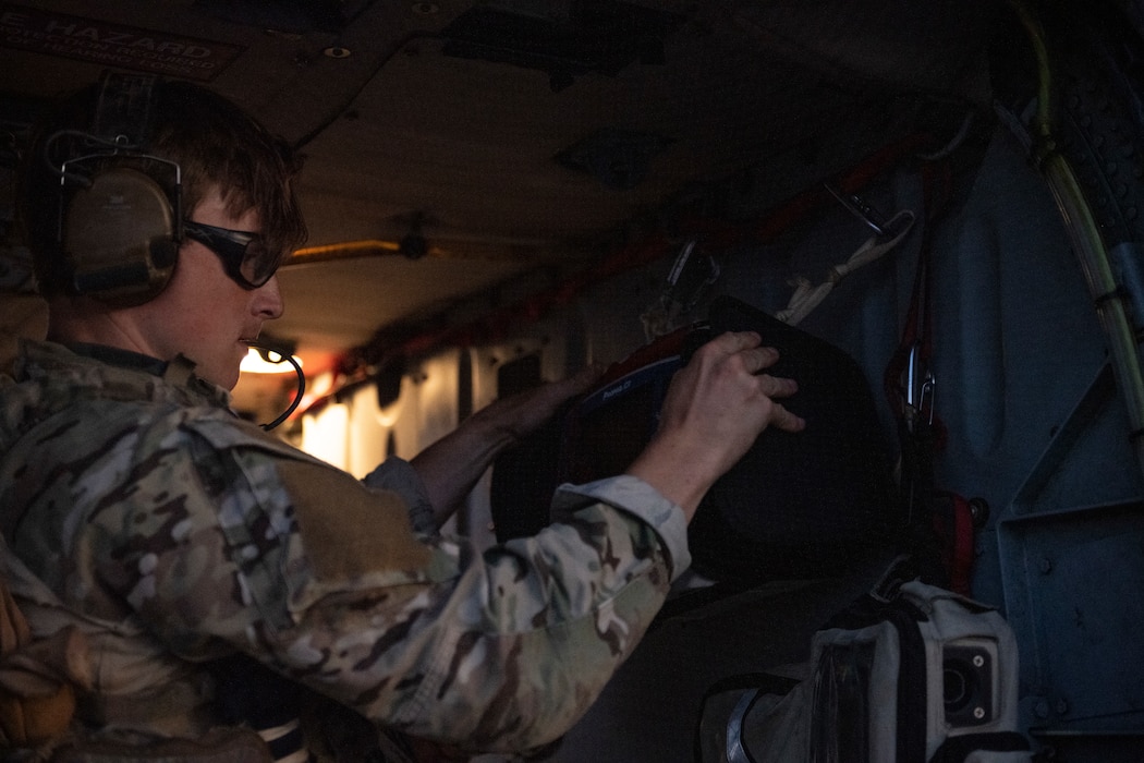 A photo of someone hanging up a heart monitor on the inside of an HH-60W Jolly Green II helicopter.