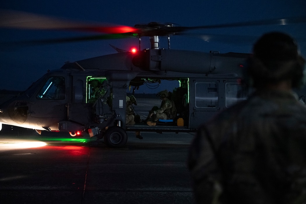 A photo of a helicopter on a flight line with glowing red and green lights on the bottom of it.