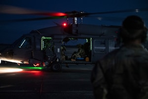 A photo of a helicopter on a flight line with glowing red and green lights on the bottom of it.