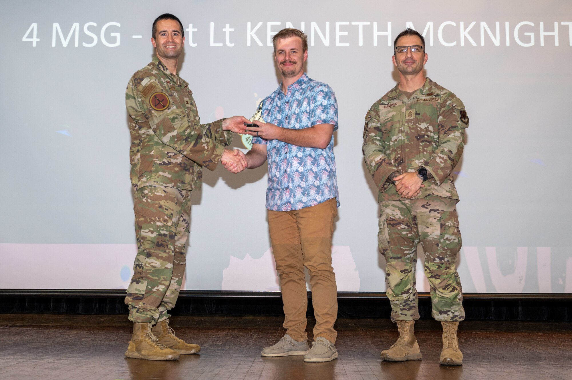 Stephen Caple, center, 4th Civil Engineer Squadron portfolio optimization chief, accepts the Junior Company Grade Officer of the 1st Quarter Award on behalf of 1st Lt. Kenneth McKnight, 4th Civil Engineer Squadron officer in charge of program development, from  Col. Morgan Lohse, left, 4th Fighter Wing commander and Chief Master Sgt. Paul Hammer, right, 4 FW command chief, during the 4 FW 1st Quarter Awards ceremony at Seymour Johnson Air Force Base, North Carolina, May 3, 2024. Quarterly Awards are awarded to Airmen and civilians in 13 different categories including Airman of the Quarter, Key Spouse of the Quarter and many more. (U.S. Air Force photo by Airman Rebecca Tierney)