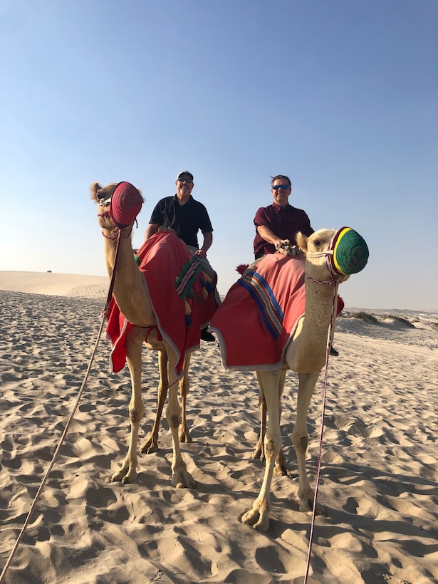 Two men sit atop camels in the desert.