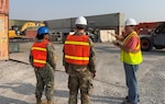 Three individuals have discussion in scrap yard