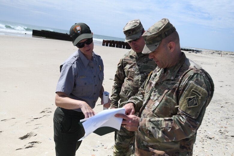During a visit to former Buxton Naval Facility, a Formerly Used Defense Site located in Dare County, North Carolina, near the Buxton Beach access May 1, 2024, National Park Service Chief of Resource Management and Science for the Cape Hatteras area, Meaghan Johnson, shows Col. Matthew McCulley, South Atlantic Division deputy commander; Col. Ron Sturgeon, Savannah District, commander, where pipes and foundations were exposed during storm events using old photos since the structures are no longer exposed and were covered with sand once again.