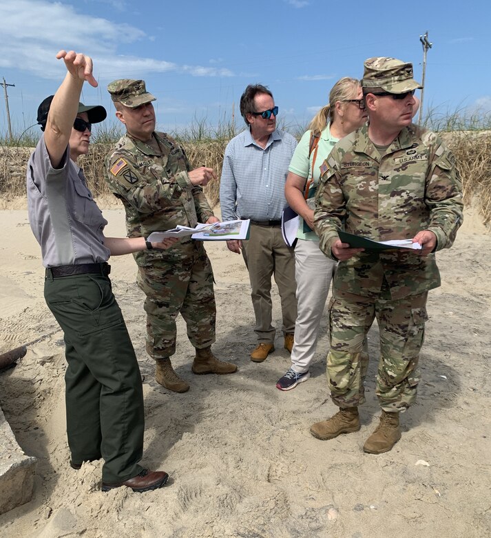 During a visit to former Buxton Naval Facility, a Formerly Used Defense Site located in Dare County, North Carolina, near the Buxton Beach access May 1, 2024, National Park Service Chief of Resource Management and Science for the Cape Hatteras area, Meaghan Johnson, shows Col. Matthew McCulley, South Atlantic Division deputy commander; Col. Ron Sturgeon, Savannah District, commander; Sandy Gibson, South Atlantic Division, Senior Environmental Program manager and Glenn Marks, Savannah District Reimbursable Branch chief, where pipes and foundations were exposed during storm events using old photos since the structures are no longer exposed and were covered with sand once again.