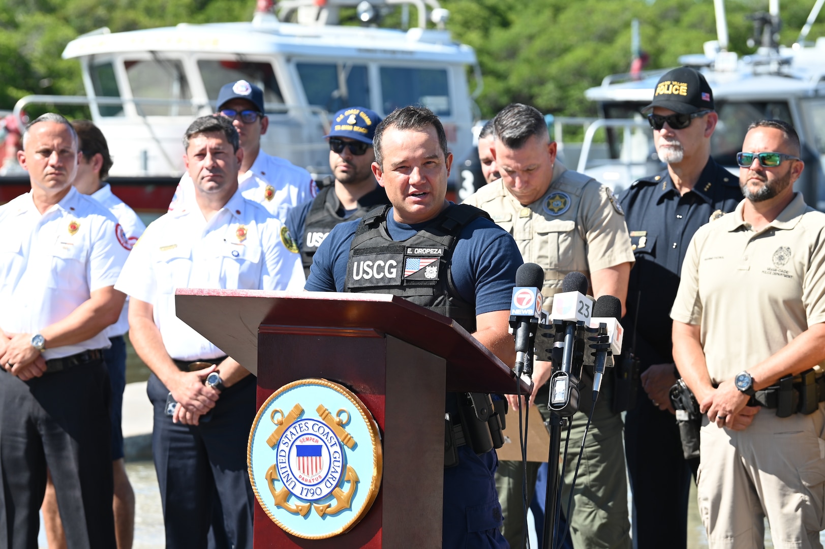 A Coast Guard Lt. Cmdr. speaks to a group in front of a podium.
