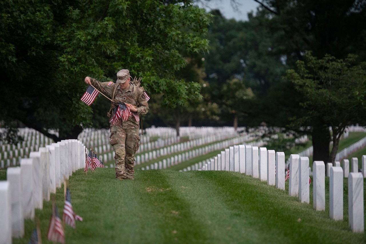 A soldier places U.S. flags at Arlington National Cemetery gravesites.