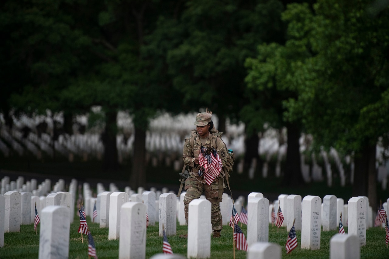 A soldier places U.S. flags at Arlington National Cemetery gravesites.