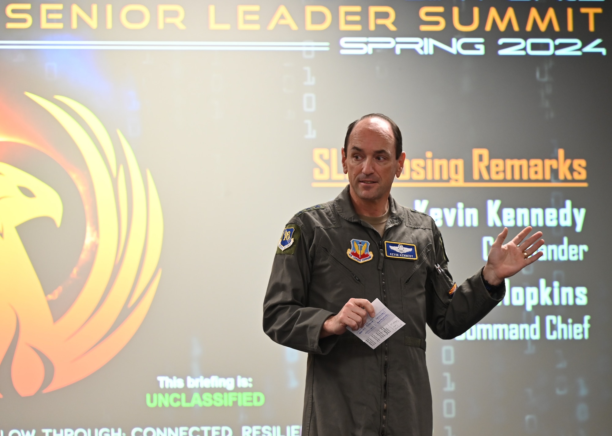 General Kennedy talks to a group of leaders in a large conference room.