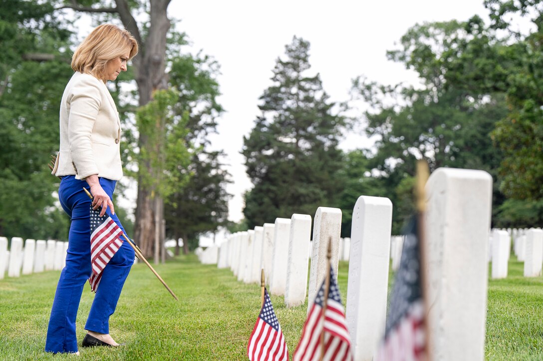Deputy Defense Secretary Kathleen Hicks holds a small U.S. flag while looking at a small white headstone in a cemetery.
