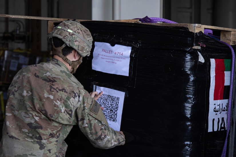 A soldier attaches a piece of paper to a pallet of humanitarian assistance cargo.