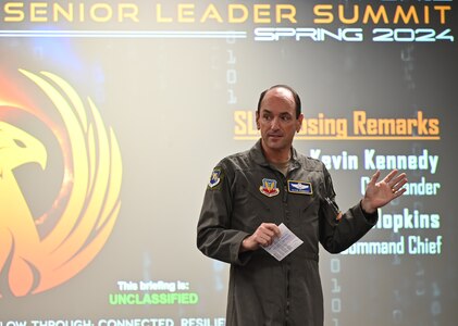 General Kennedy talks to a group of leaders in a large conference room.