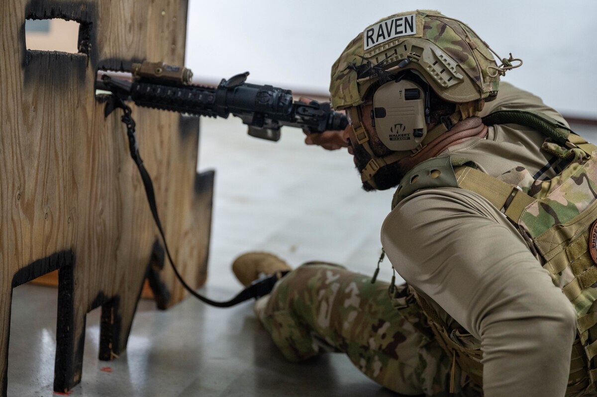 Airmen aims weapon past wooden board.