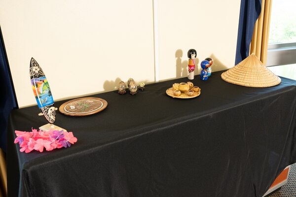 A display with a woven hat, dolls, a serving set, miniature surf board and pink flower lei