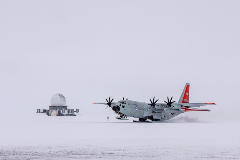 A large military aircraft with skis takes off in the snow.