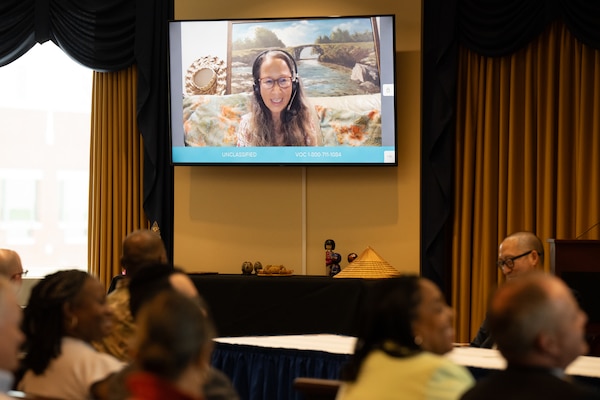 Vivian Kim is shown on a TV screen addressing a room full of seated people