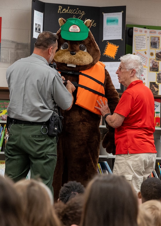 Two men putting a life jacket on a mascot.