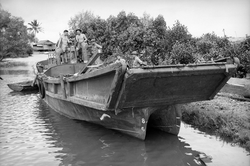 People stand atop a landing craft in a jungle setting.