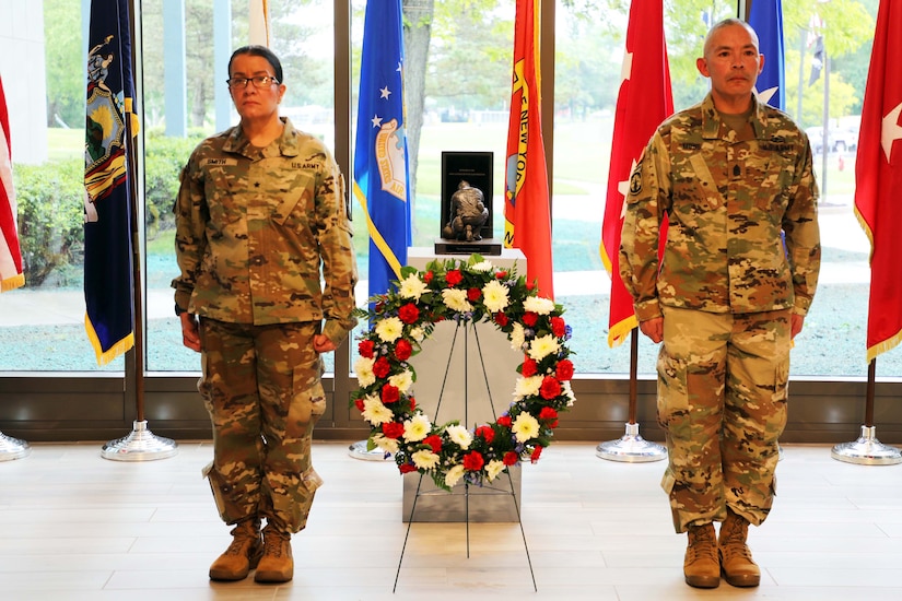 Two military officers stand at attention on both sides of a wreath.