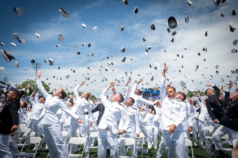 Nearly commission sailors and marines throw their midshipmen covers during a graduation ceremony.