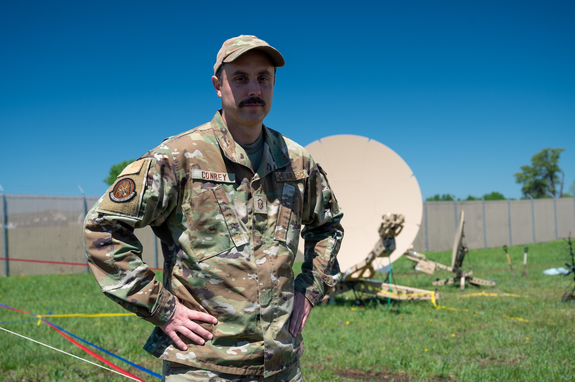 U.S. Air National Guard Airman in OCP pattern uniform poses in front of a 2.4 meter satellite dish.
