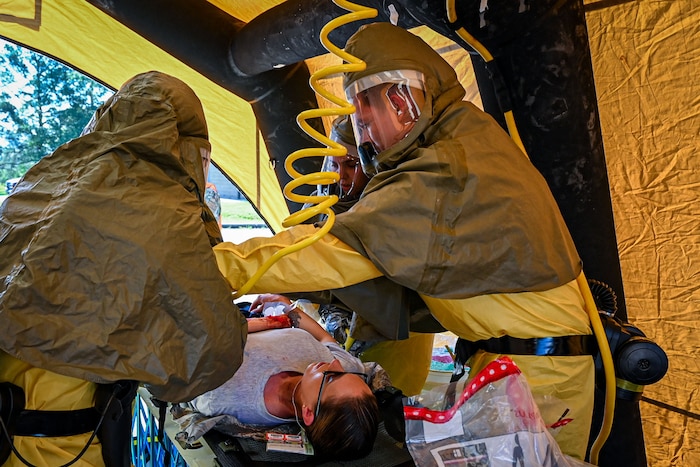 Three military members spray water on a patient to simulate a Medical exercise.