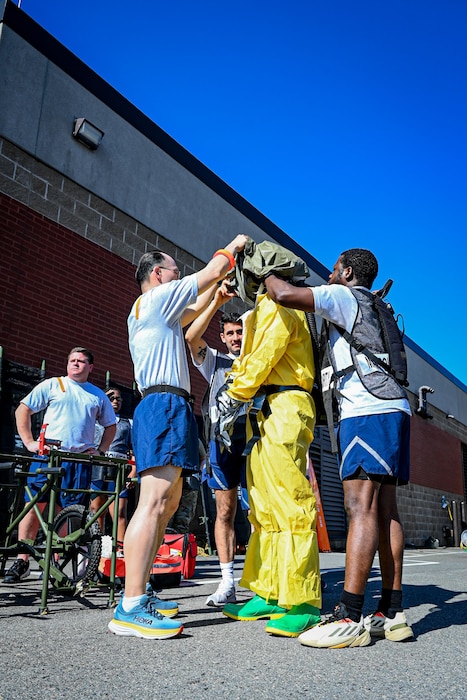 Three military members help another member put on his helmet to simulate a Medical exercise.