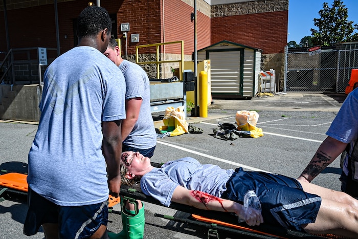 Three military members carry a patient to simulate a Medical exercise.