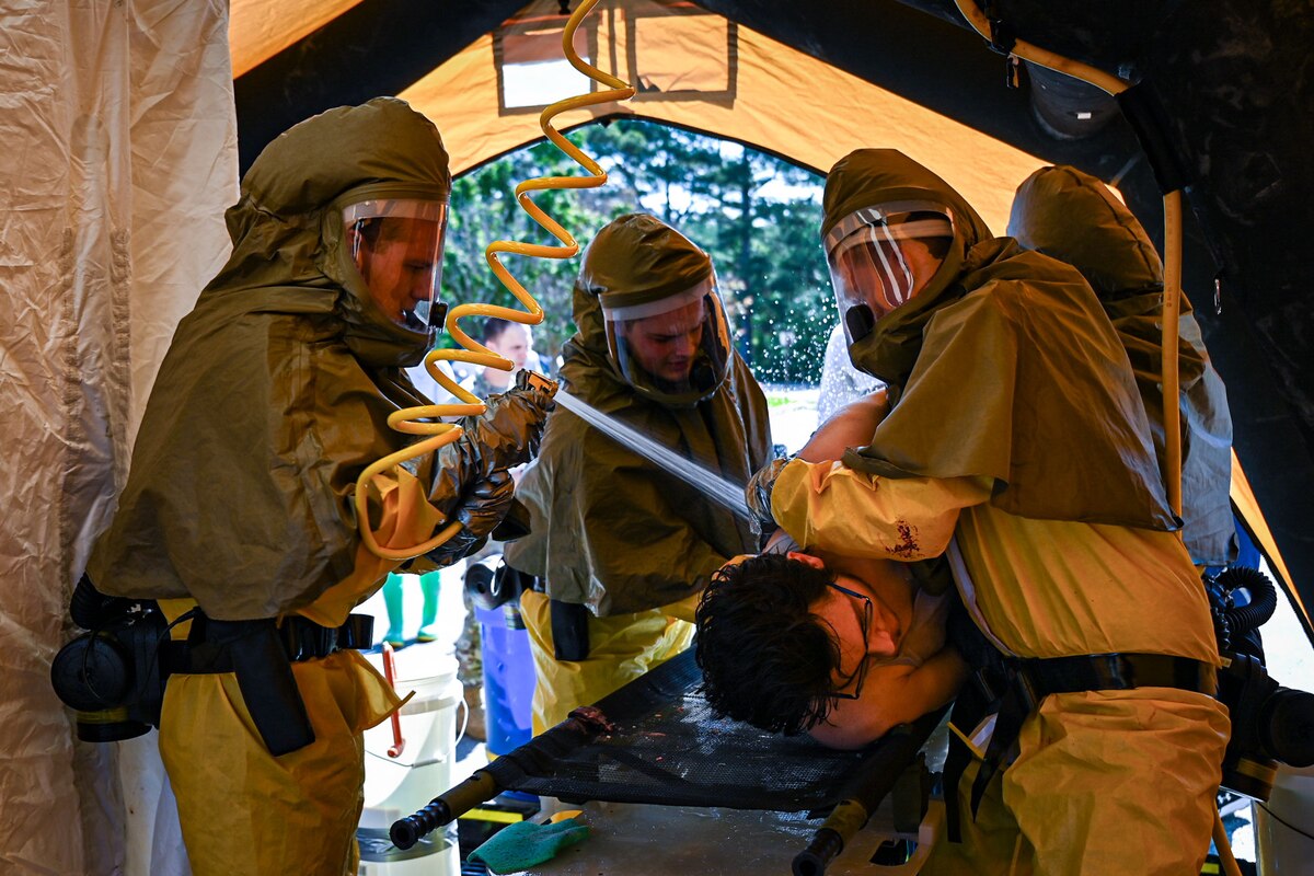 Four military members spray water on a patient to simulate a Medical exercise.