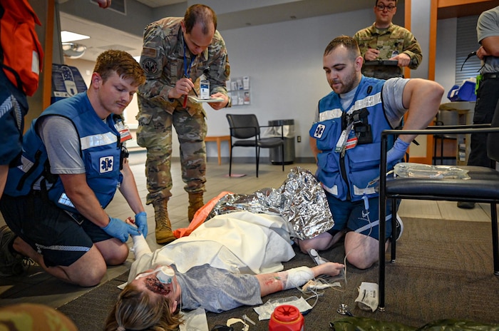 Three military members stand over a patient to simulate a Medical exercise.