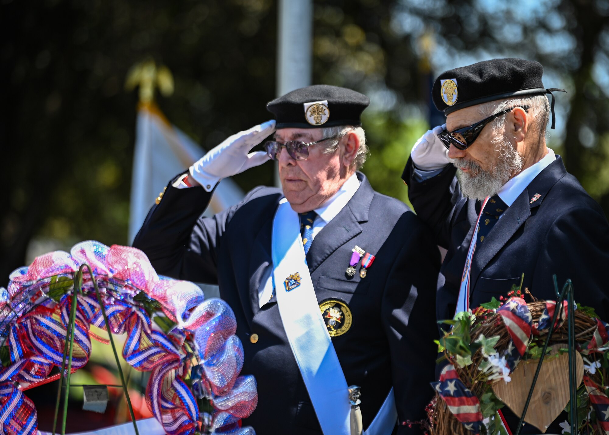 Two veterans salute a wreath.